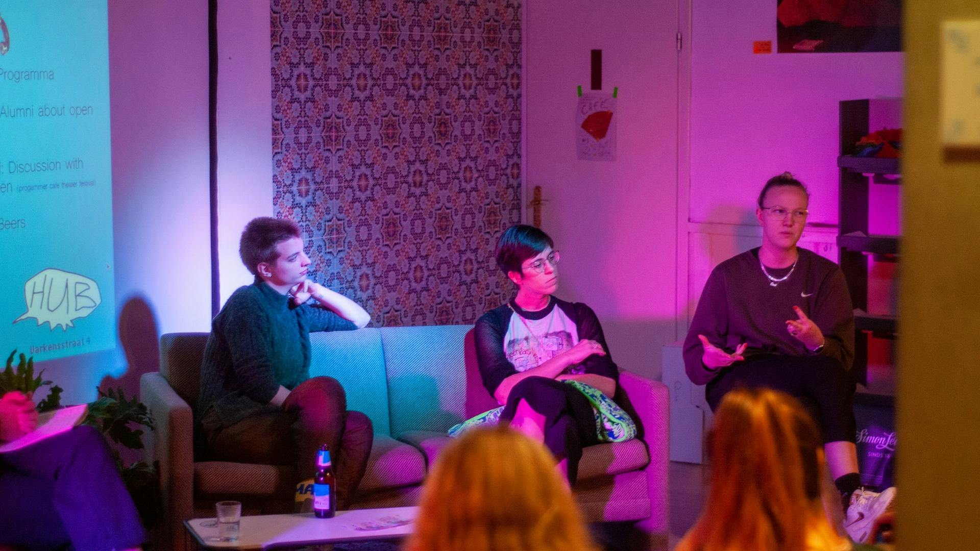 Foto van een avond in The Hub, waarbij drie mensen op het podium samen aan het woord zijn.