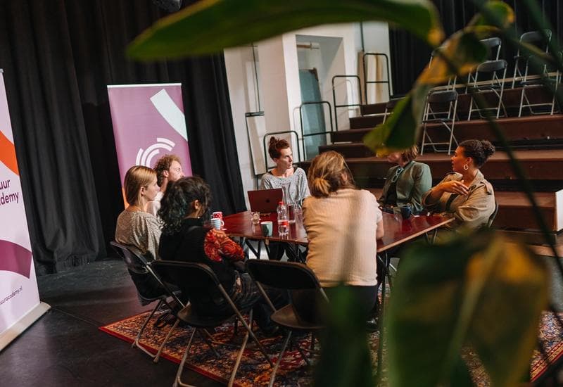 Foto van zeven mensen aan een tafel met elkaar in gesprek tijdens een programma van Cultuur Academy